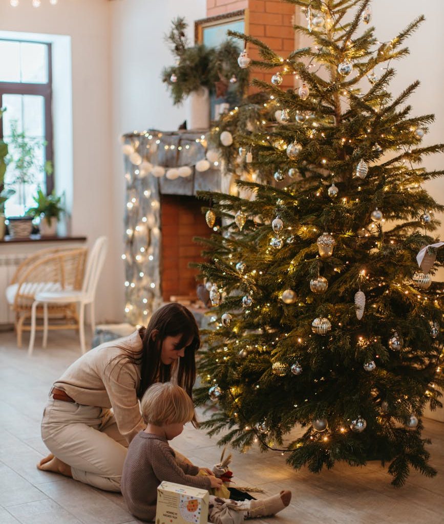 a child sitting next to a christmas tree with his mom