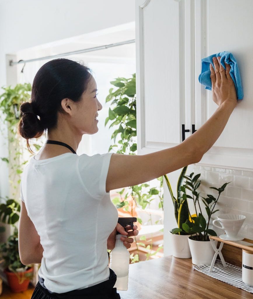 a woman wiping the surface of a cabinet