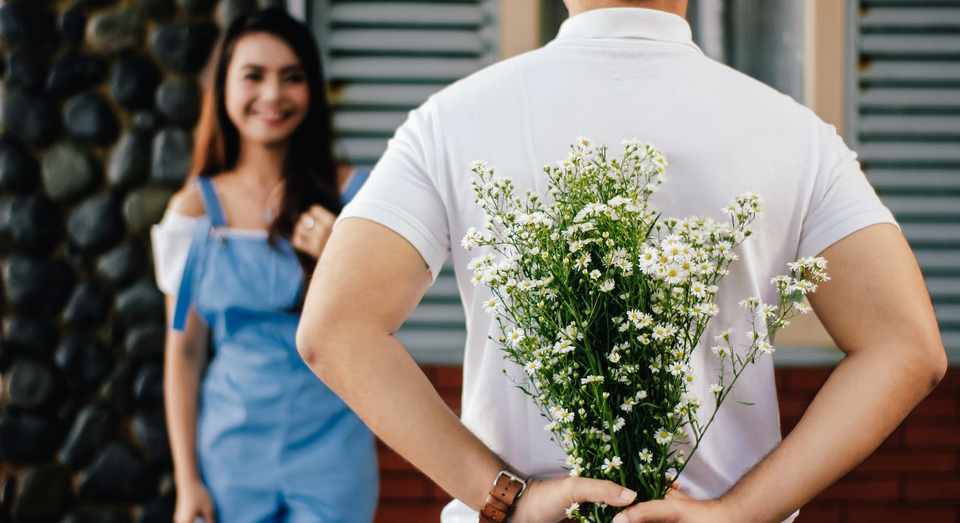 man holding baby s breath flower in front of woman standing near marble wall